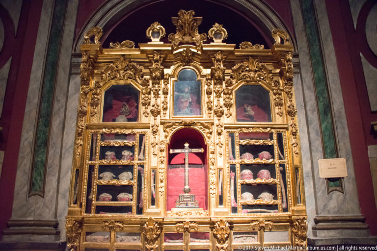 Ornate gilded reliquary display with a central cross, small relic compartments, painted panels, and dense carved decoration.