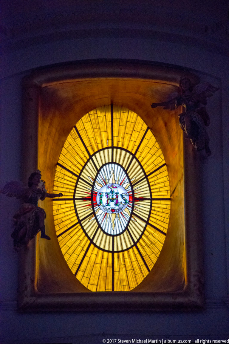 Circular amber stained-glass window with radiating panes and a small multicolored medallion at the center.
