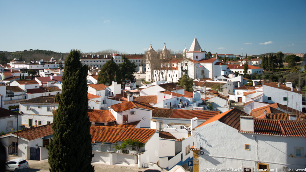 Panorama of white houses and terracotta roofs with cypress trees and several church towers rising above Vila Viçosa.