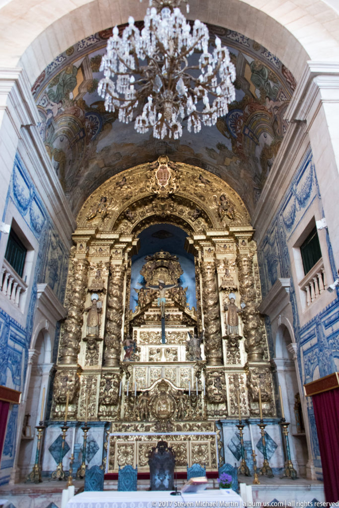 Ornate gilded sanctuary with central crucifix, painted vault and blue-and-white azulejo panels along both side walls.