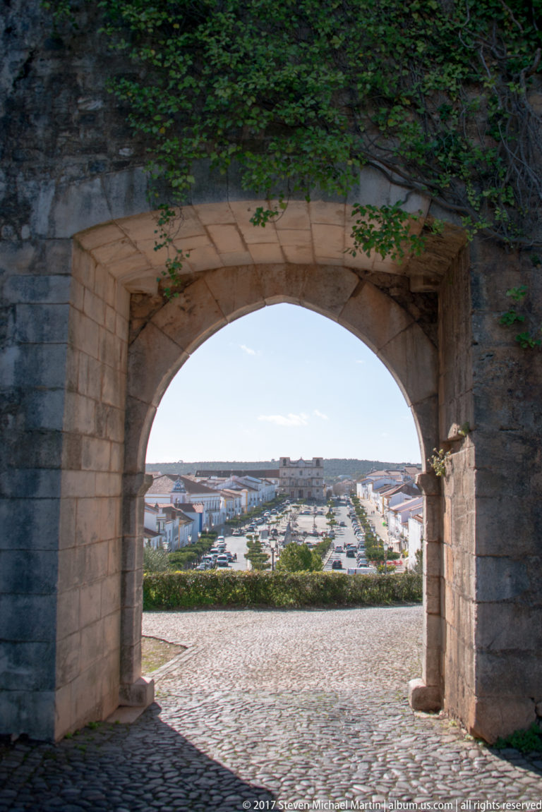 Large stone archway and cobbled passage framing a distant view over whitewashed Vila Viçosa.