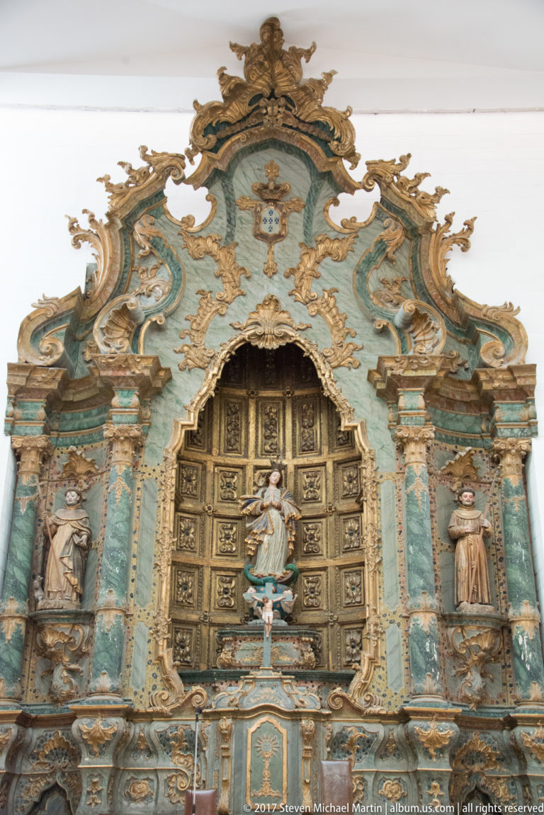 Close view of an ornate turquoise and gilded altarpiece with central statue, side figures and dense scrolling carving.