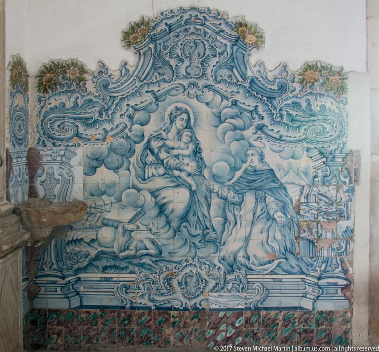 Blue-and-white tiled devotional scene of the Virgin and Child in clouds facing a kneeling figure, framed by ornate scrollwork.
