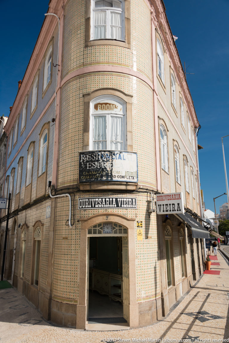 Azulejo-clad corner building with Ourivesaria Vieira signs, curved upper façade, balconies, and an open jewelry-shop entrance.