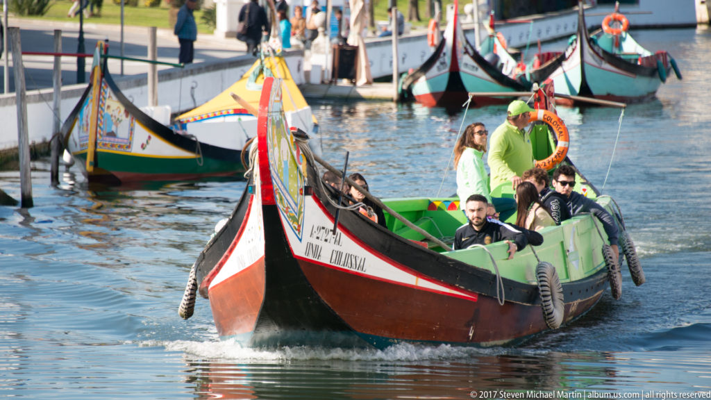 Colorful passenger moliceiro approaching on a canal with several other traditional boats moored behind it.