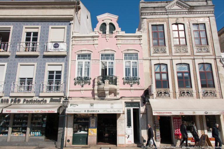 Three adjoining historic façades in blue tile, pink stucco, and cream patterned tile above ground-floor shops in Aveiro.