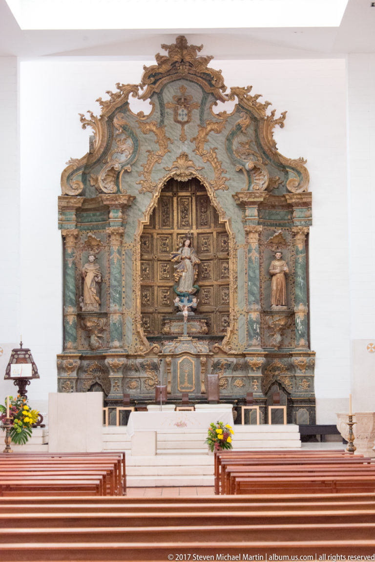 Church interior with wooden pews facing an ornate turquoise, gold and carved altarpiece centered on a small devotional statue.