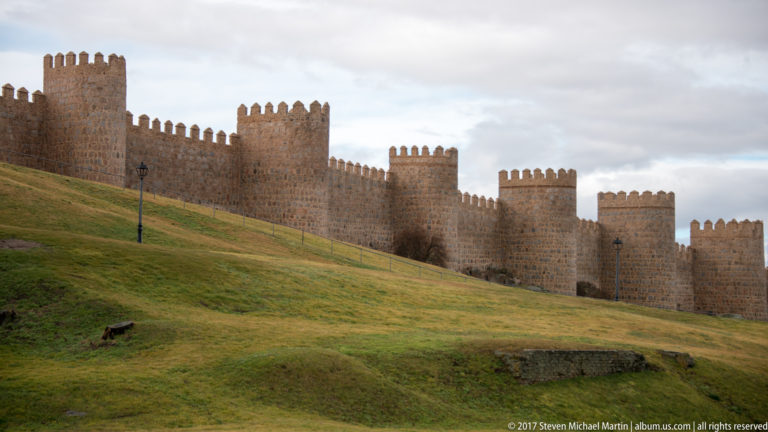Long line of Ávila’s crenellated stone walls and towers crossing a broad grassy slope.
