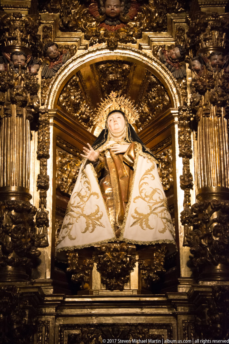 Close view of Saint Teresa of Ávila in Carmelite habit and white mantle within a gilded altar niche.