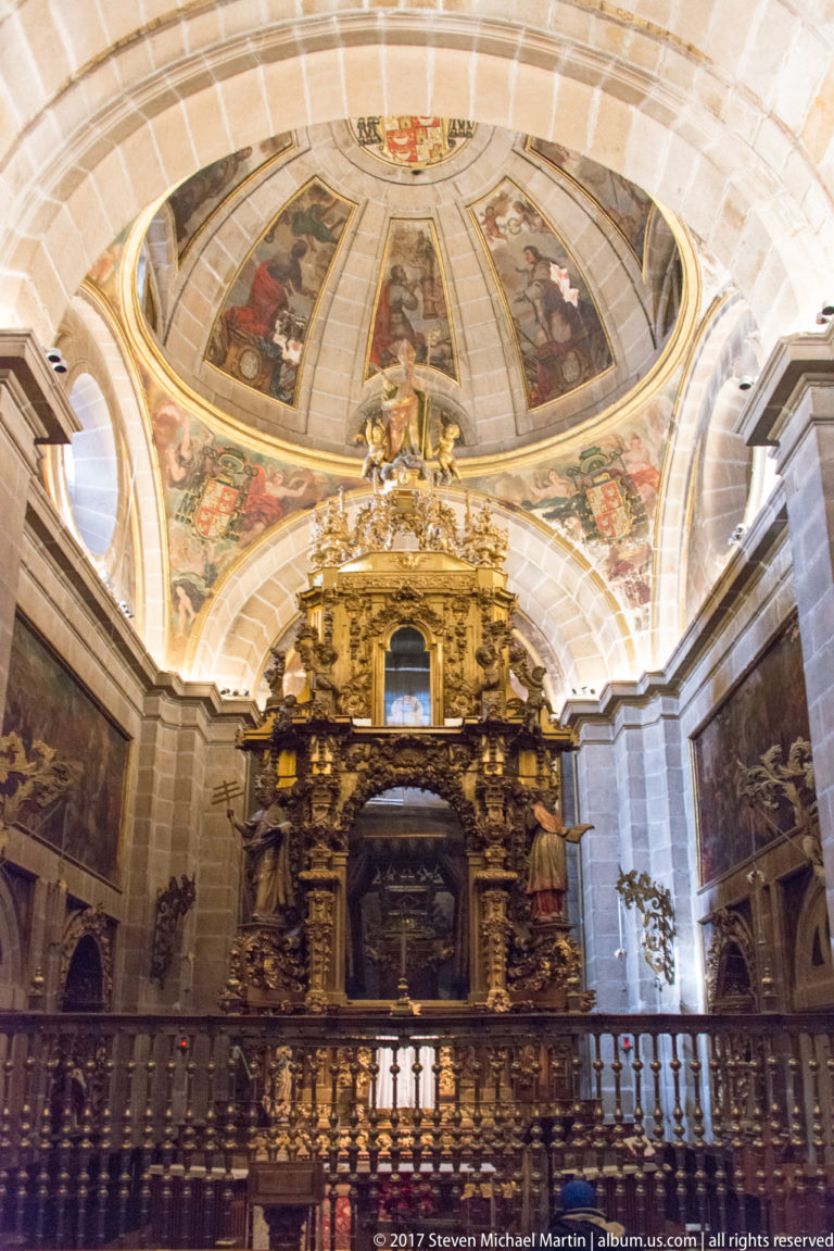 Gilded Baroque structure behind a wooden gallery rail beneath a frescoed vaulted church ceiling.