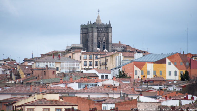 Ávila rooftops clustered below a large square stone church or cathedral tower with pinnacles.