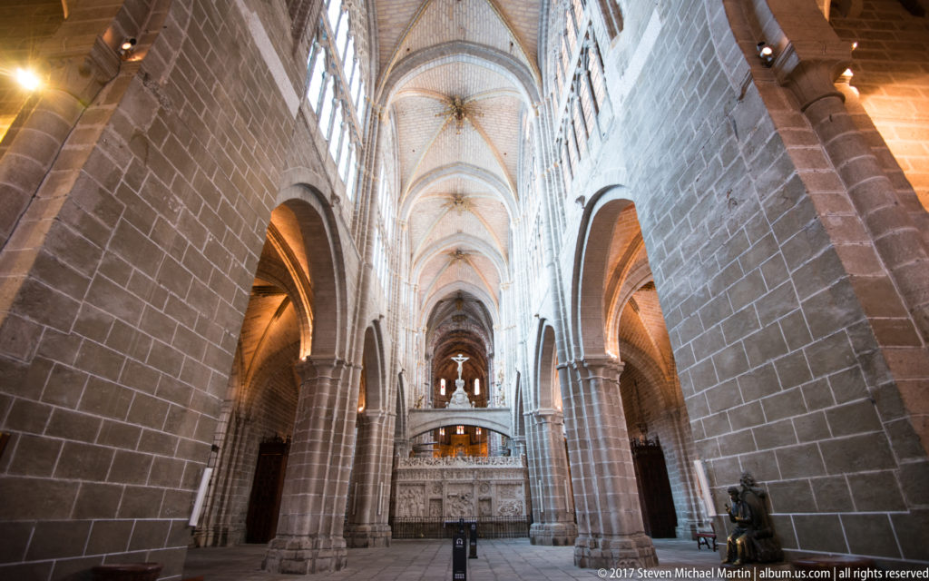 Long view down the Gothic nave of Ávila Cathedral with massive stone piers, pointed arches and ribbed vaults.
