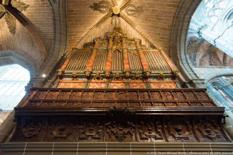 Historic pipe organ above a richly carved wooden choir gallery beneath Gothic vaulting in Ávila Cathedral.