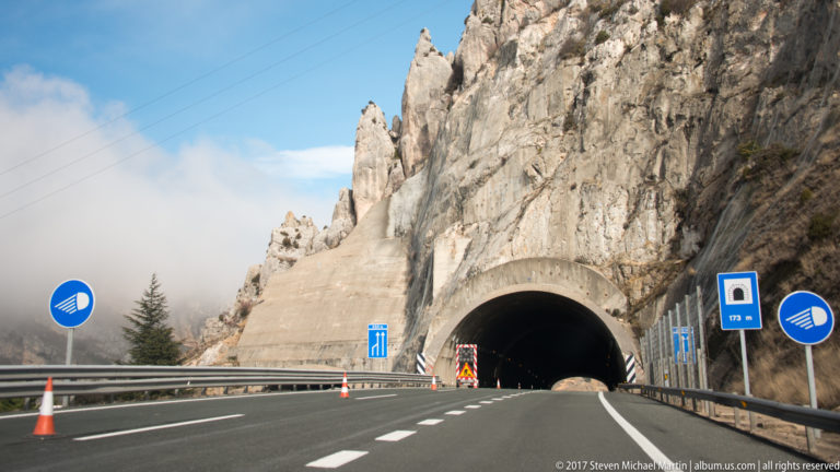 Multi-lane highway entering a large tunnel portal beneath a steep exposed rock face near Bilbao.