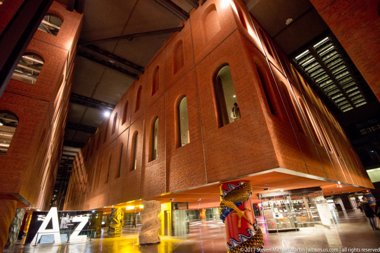 Low-angle view inside Azkuna Zentroa of a large brick volume raised on decorative columns above shops and public circulation.