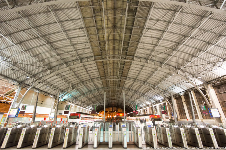 Bilbao-Abando station concourse with rows of ticket gates beneath a vast arched metal train-shed roof.