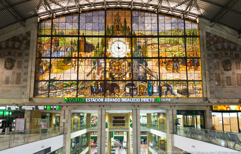 Large stained-glass mural and central clock above the signed Estación Abando Indalecio Prieto concourse in Bilbao.