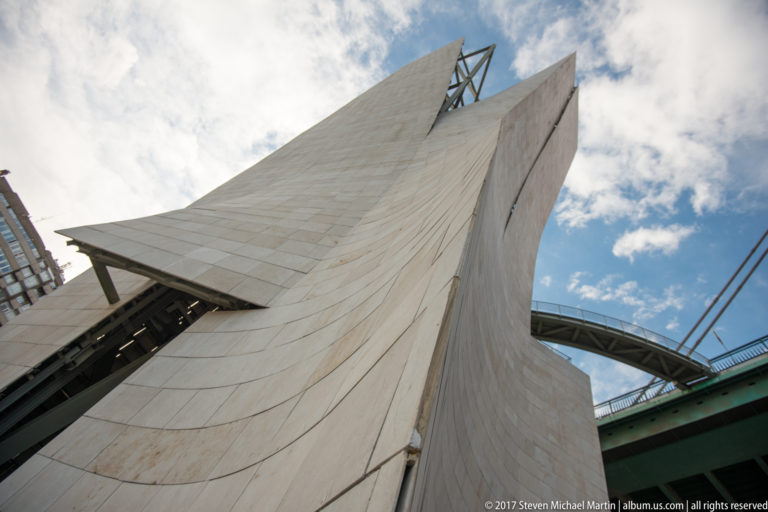 Low-angle close view of a pale angular bridge support beside the green deck and cables of La Salve Bridge.