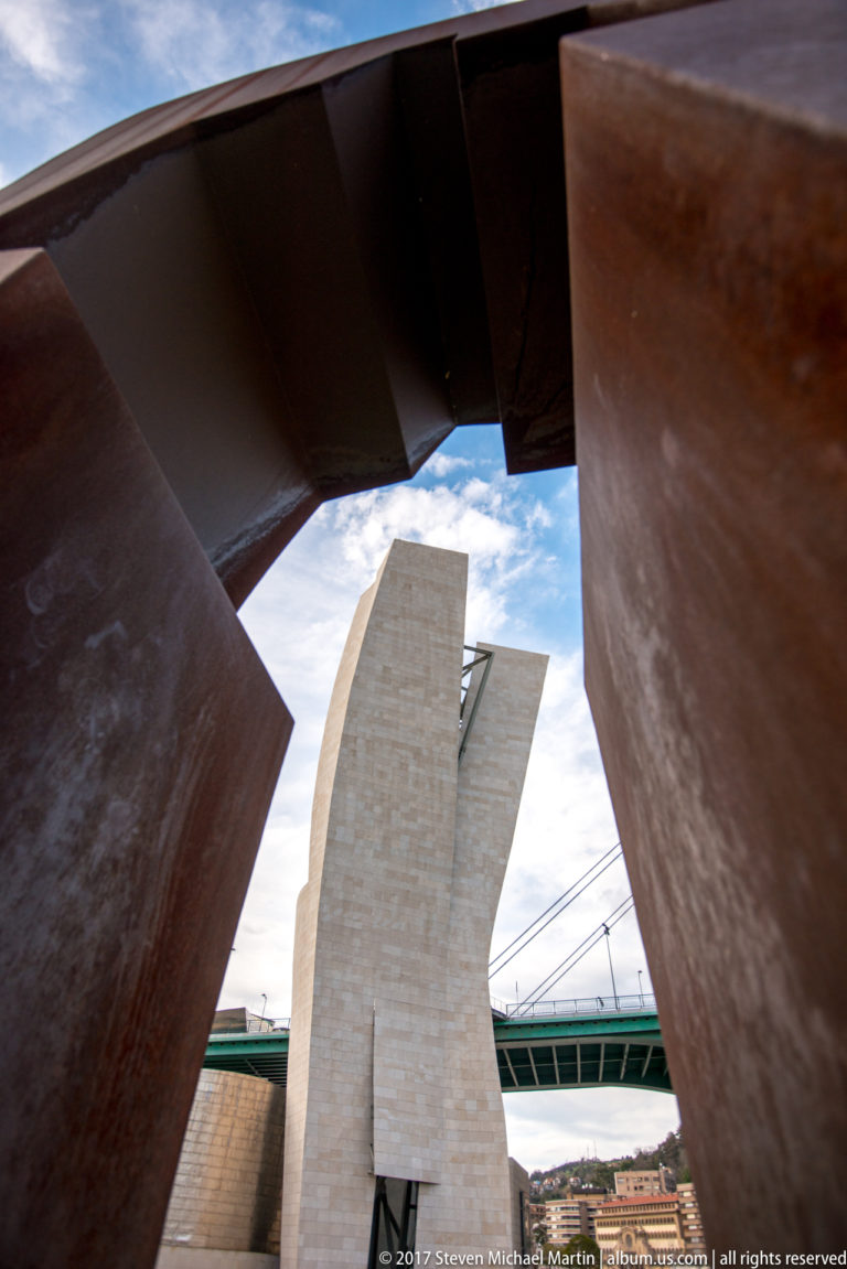 Pale La Salve Bridge support framed through the opening of a massive rusted-steel sculpture.