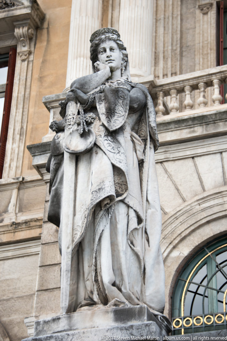 Stone allegorical female figure in classical drapery mounted on the ornate façade of Bilbao City Hall.