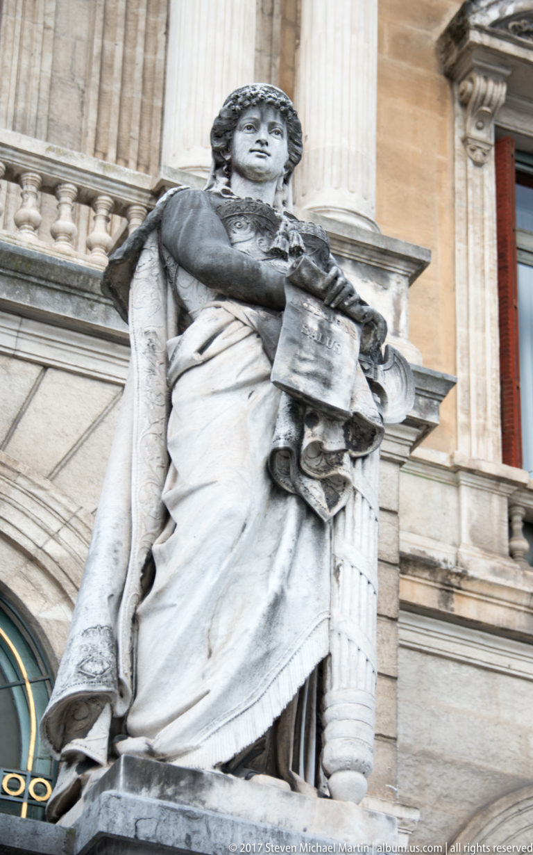 Close low-angle view of a draped stone female allegorical figure on Bilbao City Hall, holding an object across her torso.
