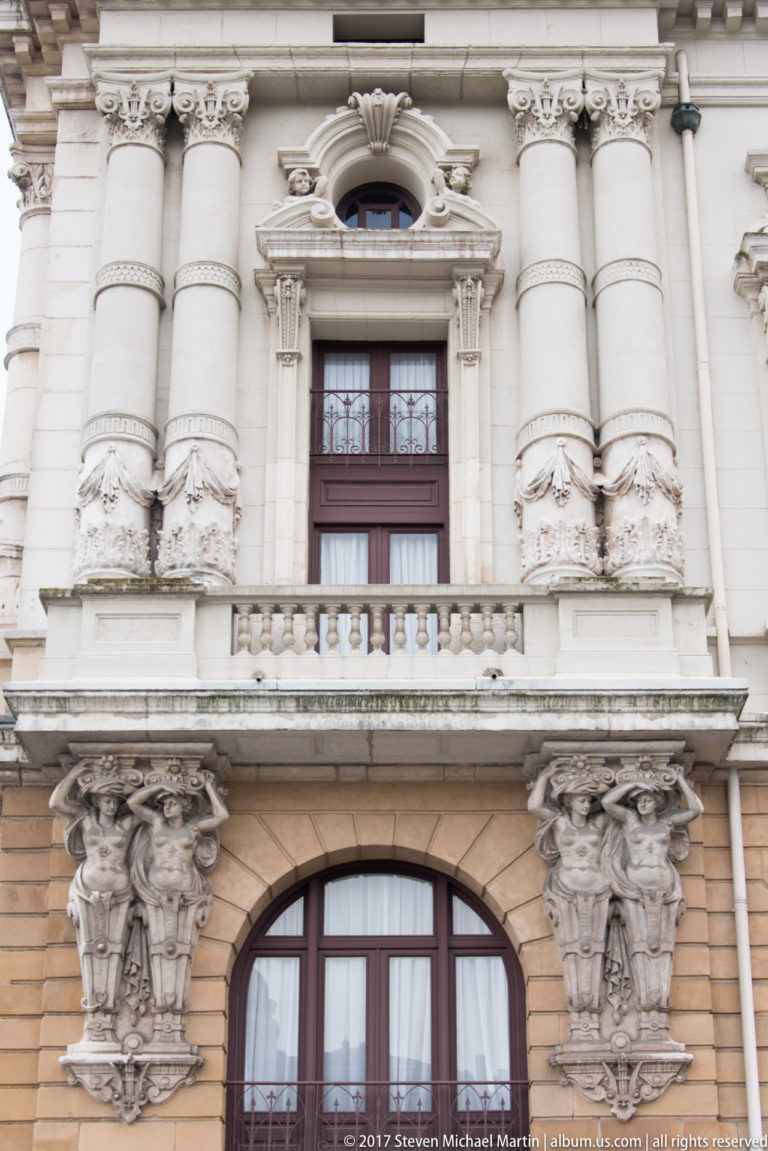 Ornate Teatro Arriaga window bay with paired sculptural supports, arched glazing, stone balustrade, and clustered columns.
