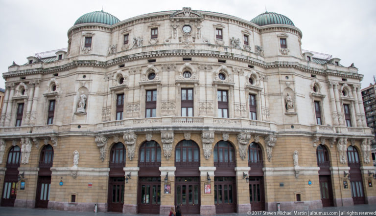 Wide view of Teatro Arriaga’s ornate rounded façade with arched openings, sculpture, balustrades, and a dark domed roof.