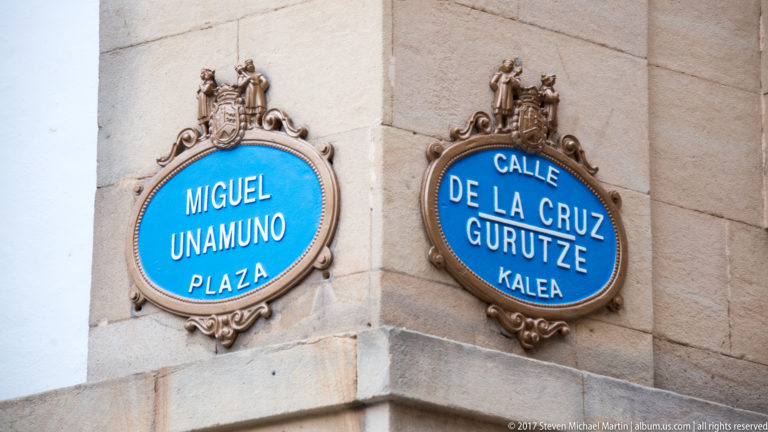 Blue decorative street plaques read “Miguel Unamuno Plaza” and “Calle de la Cruz / Gurutze Kalea” on a stone corner.
