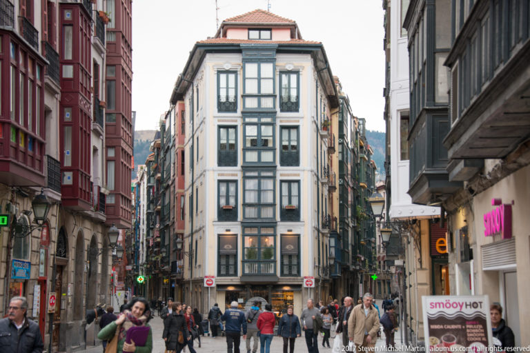 Pedestrians fill a narrow Casco Viejo street lined with colorful multi-story buildings, balconies, bay windows, and shops.