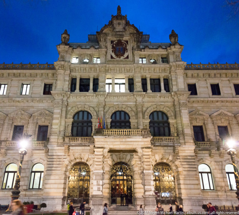 Illuminated stone façade of the Palacio de la Diputación Foral de Bizkaia at night, with arched entrances and a central crest.