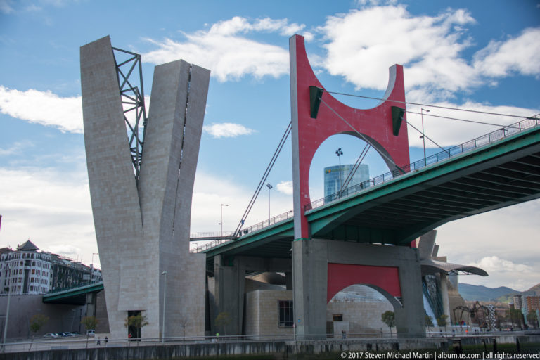 Close view of La Salve Bridge showing its red portal, concrete support, green deck, and suspension elements.