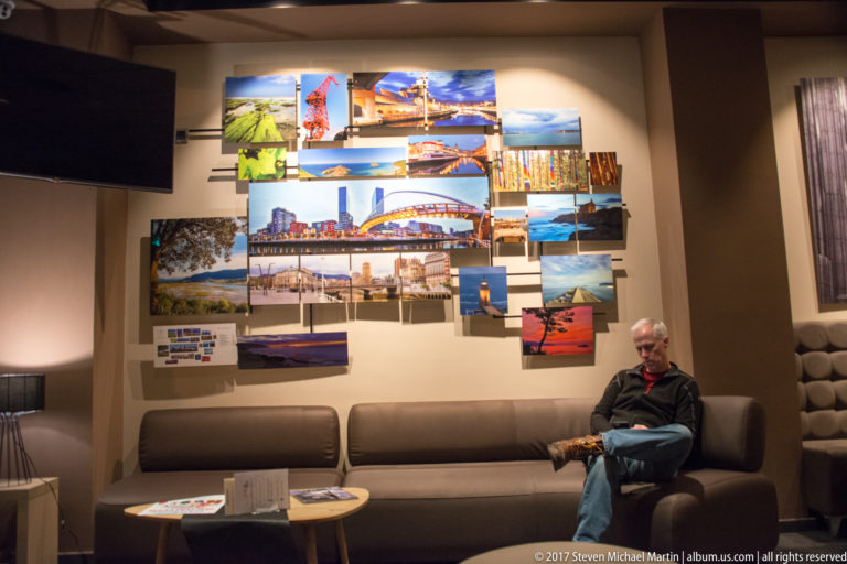 Person seated on a sofa in a hotel-style lounge beneath a wall collage of colorful Bilbao city photographs.