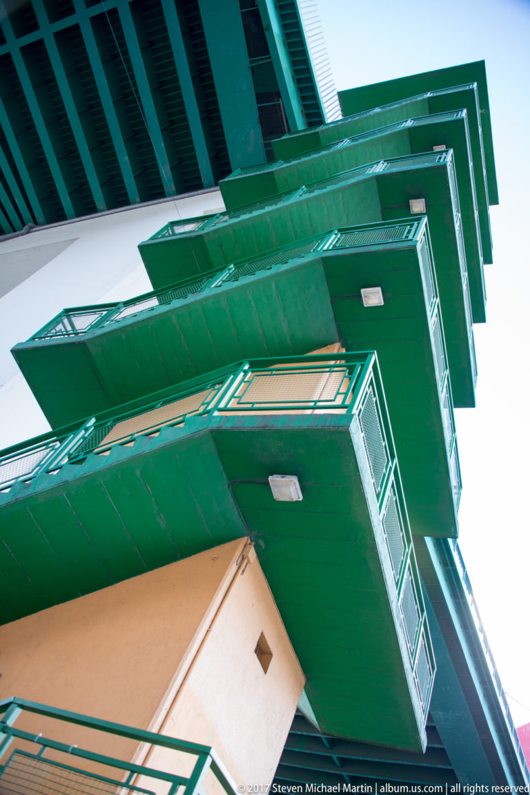Upward view of stacked green metal landings and railings projecting from a yellow bridge access structure.