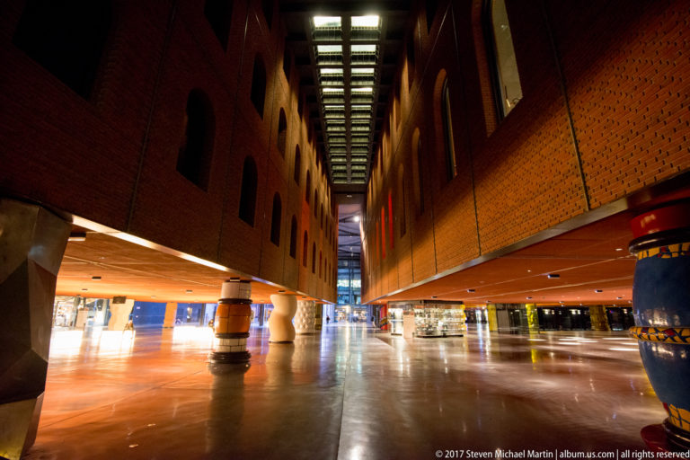 Azkuna Zentroa interior with suspended brick-clad volumes, decorated columns, polished floor, and a long illuminated ceiling strip.