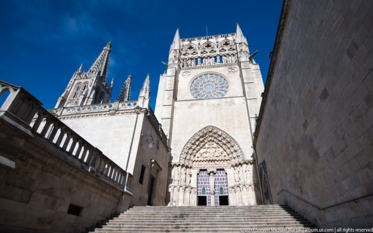 Stone steps rise to a sculpted Gothic portal beneath a large rose window on Burgos Cathedral.