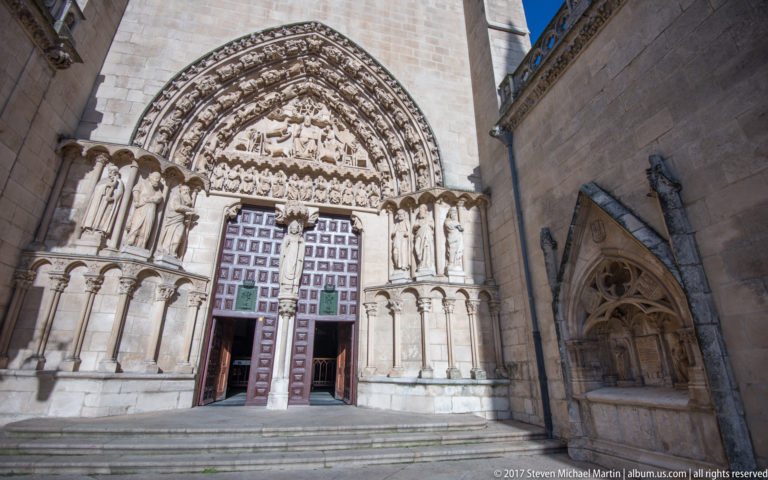 Close view of Burgos Cathedral portal with sculpted standing figures, carved tympanum, archivolts, and open paneled doors.