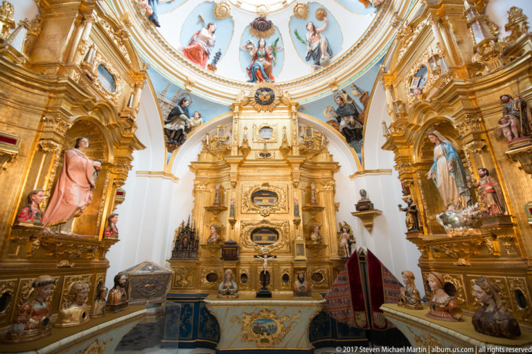 Ornate cathedral chapel filled with gilded altarpieces, sculpted saints, painted ceiling figures, and altar furnishings.