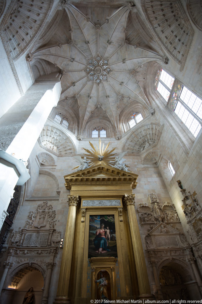 Low-angle cathedral interior with framed altar painting, carved wall monuments, high windows, and star-patterned rib vault.