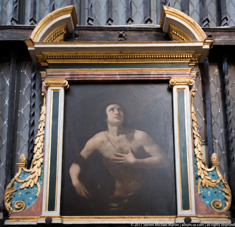 Dark religious painting of a bare-chested man looking upward, set in an ornate black, gold, blue, and red frame.