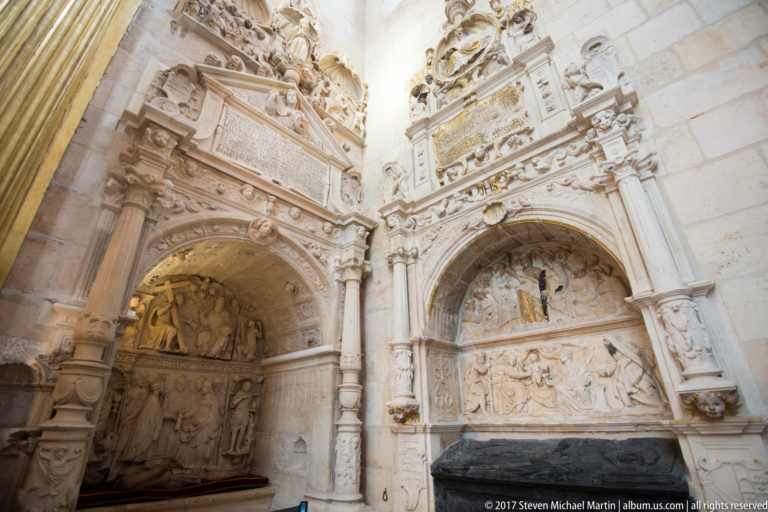 Two ornate pale stone wall monuments with arches, columns, inscriptions, heraldry, and carved narrative reliefs.