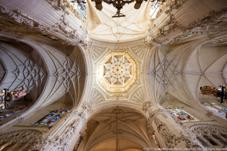 Upward view of Burgos Cathedral ceiling with luminous star-shaped central lantern, radiating ribs, tracery, and surrounding vault bays.