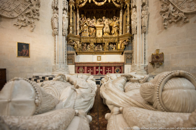 Two recumbent carved tomb effigies in the foreground with a gilded chapel altarpiece behind.