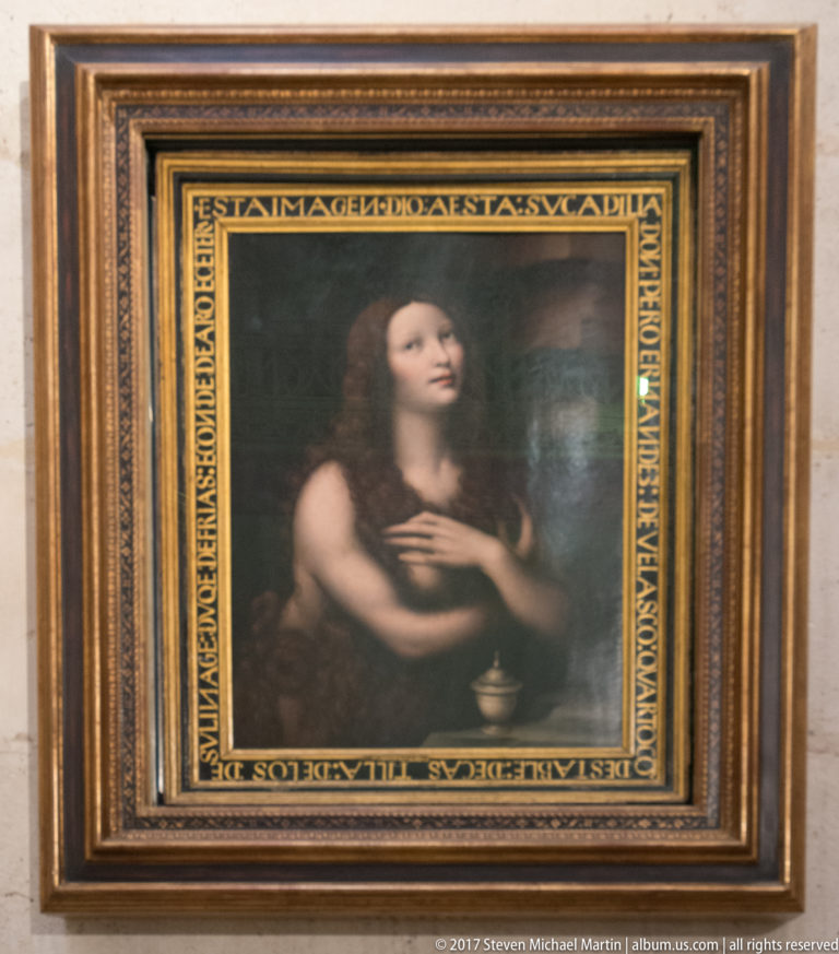Framed devotional painting of a young woman with crossed hands looking upward against a dark background.
