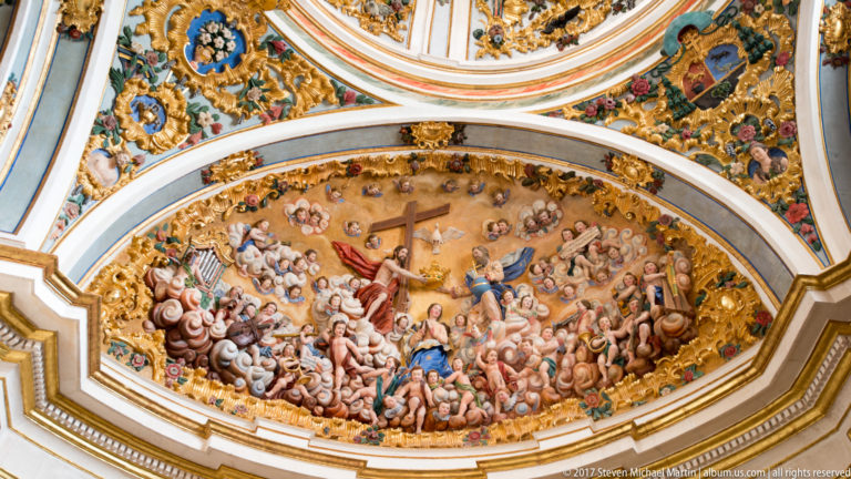 Oval ceiling painting crowded with Christ, the Virgin, angels, and figures amid clouds and gilded ornament.