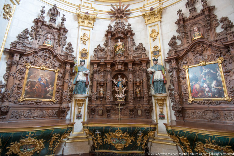 Three ornate dark-wood Baroque retables with paintings, statues, gilding, and green altar frontals.