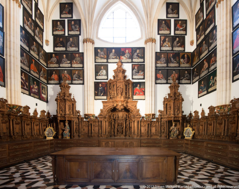 Dark carved choir stalls below walls densely hung with portraits of clergy in a bright vaulted room.