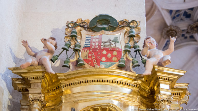 Polychrome quartered coat of arms with two putti, green ecclesiastical emblems, and gilded architectural framing.