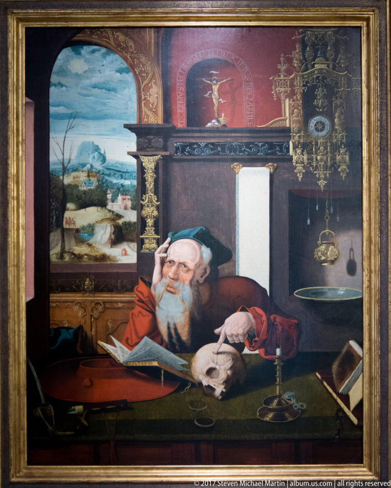 Painting of an elderly bearded scholar writing at a desk among books, papers, a balance, and instruments.