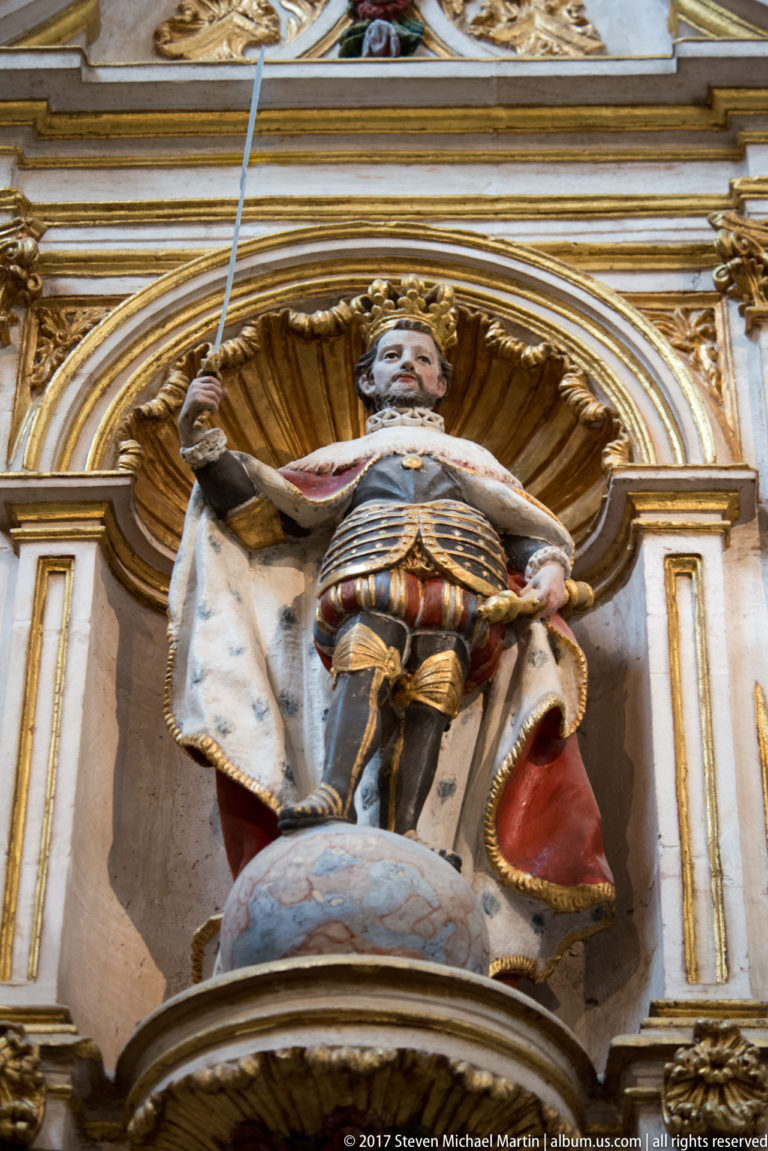Polychrome crowned man in armor and an ermine-lined mantle standing in a gilded shell niche.