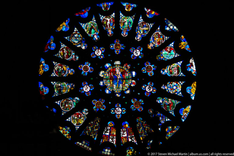 Large circular stained-glass rose window glowing in blue, red, gold, and green against a dark church interior.